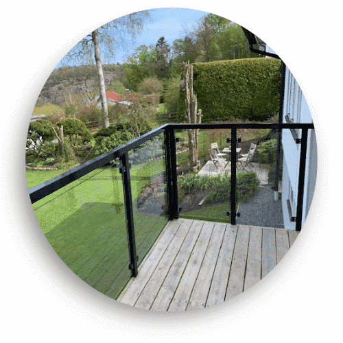 Elegantes Glasgeländer mit schwarz lackierten Aluminiumprofilen, montiert auf einer Holzterrasse in grüner Gartenumgebung.