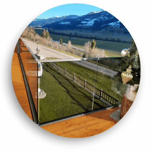 Modernes Ganzglasgeländer ohne Pfosten auf Holzterrasse installiert, mit freiem Blick auf Landschaft und schneebedeckte Berge.