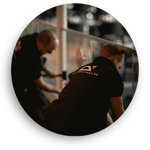 Zwei Monteure in schwarzer Arbeitskleidung installieren ein Glasgeländer in einem öffentlichen Raum. Sie arbeiten sorgfältig an der Einstellung und Montage des Glases, das durch rostfreie Befestigungselemente an Ort und Stelle gehalten wird. Spiegelungen im Glas verleihen dem Raum ein Gefühl von Weite und Transparenz.