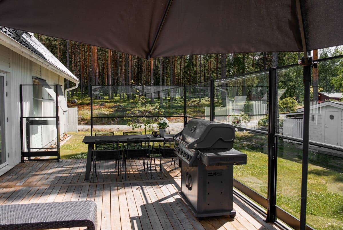 Höhenverstellbares schwarzes Aluminium-Glasgeländer um Holzterrasse mit Esstisch, Grill und Sonnenschirm im Garten am Waldrand