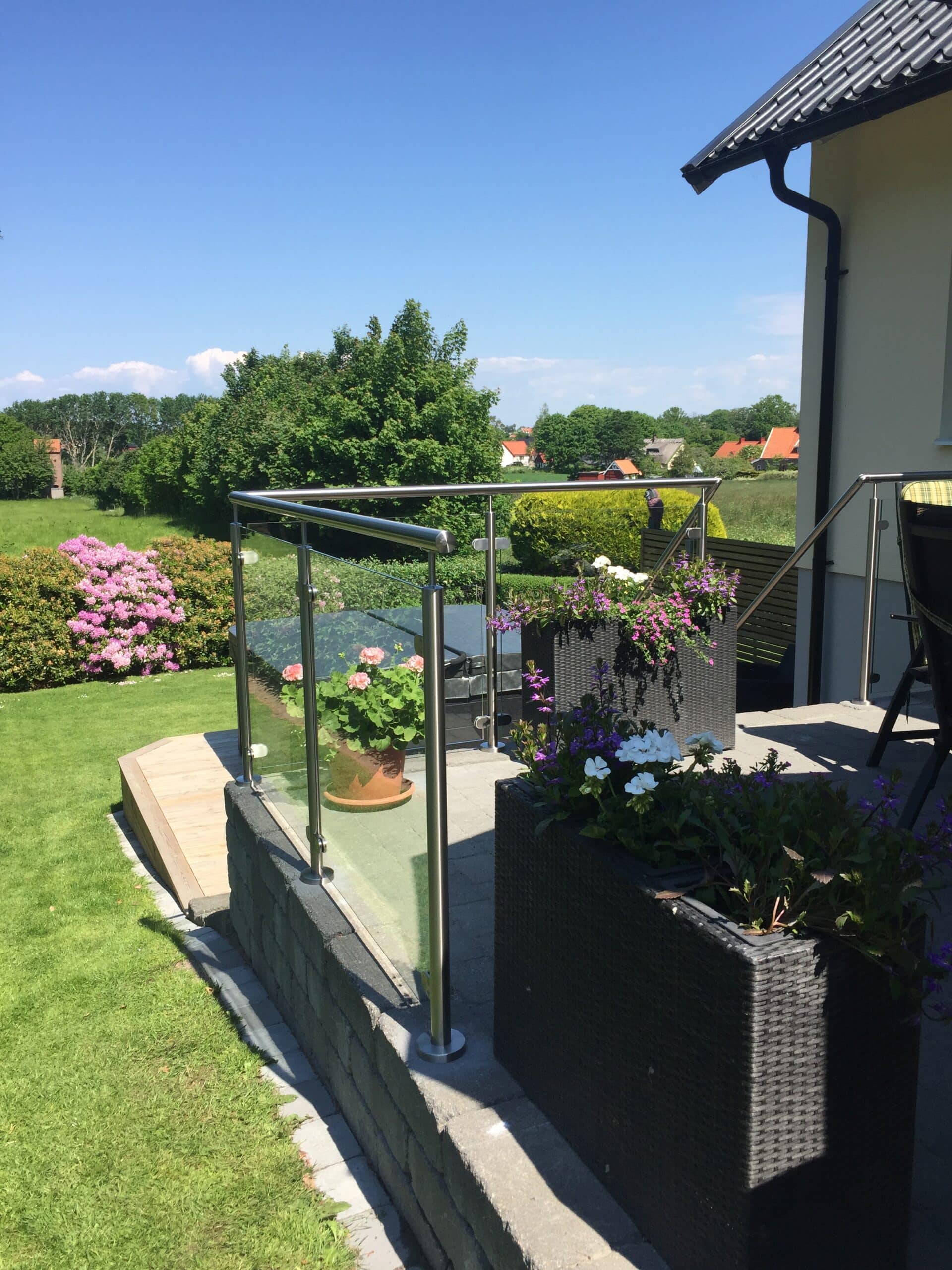 Kleine erhöhte Terrasse mit Edelstahlgeländer und Pflanzenkübeln, Blick auf gepflegten Garten