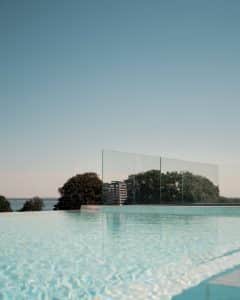 Pfostenfreies Glasgeländer am Infinity-Pool mit Blick auf das Meer und Baumkronen – für ein offenes, luxuriöses Ambiente.