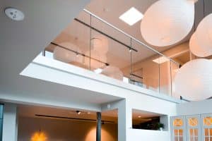 Modernes, pfostenfreies Glasgeländer montiert in einem öffentlichen Innenraum mit hoher Decke, großen Papierlampen und heller Gestaltung.